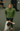 Model wearing a green Ariiston sweatshirt, standing in the middle of a busy road with moving people.